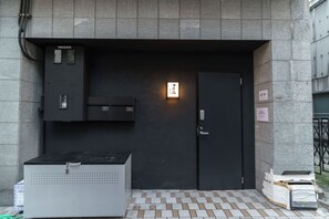 Ein Gebäudeeingang mit einer dunklen Tür, einem beleuchteten Schild und einem gefliesten Boden.