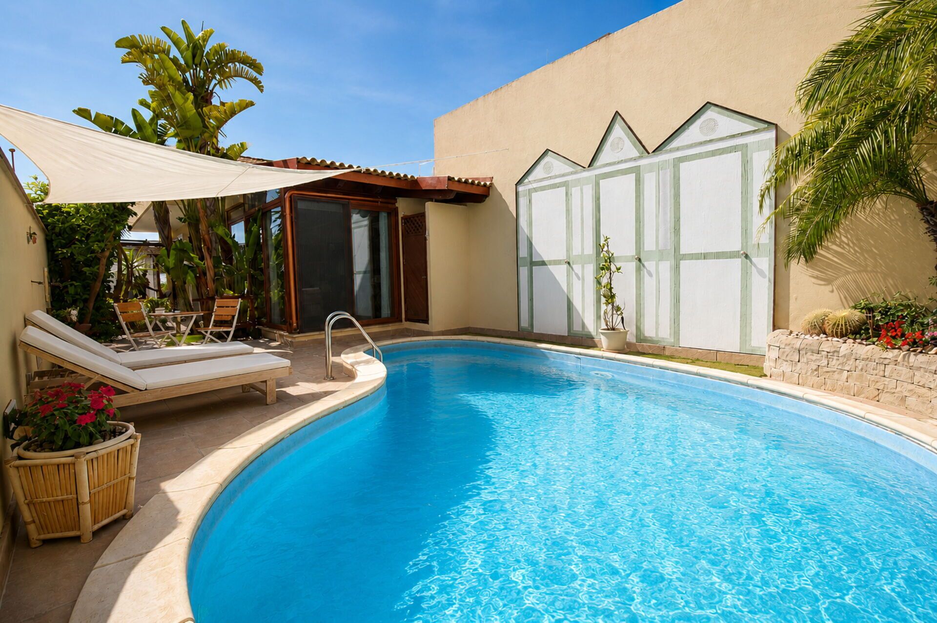 Una piscina con sillas de descanso, un ventanal y plantas tropicales.