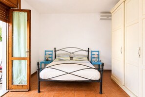 Ein Einzelbett mit Metallgestell, zwei Nachttische und ein Kleiderschrank in einem Zimmer mit Fliesenboden.