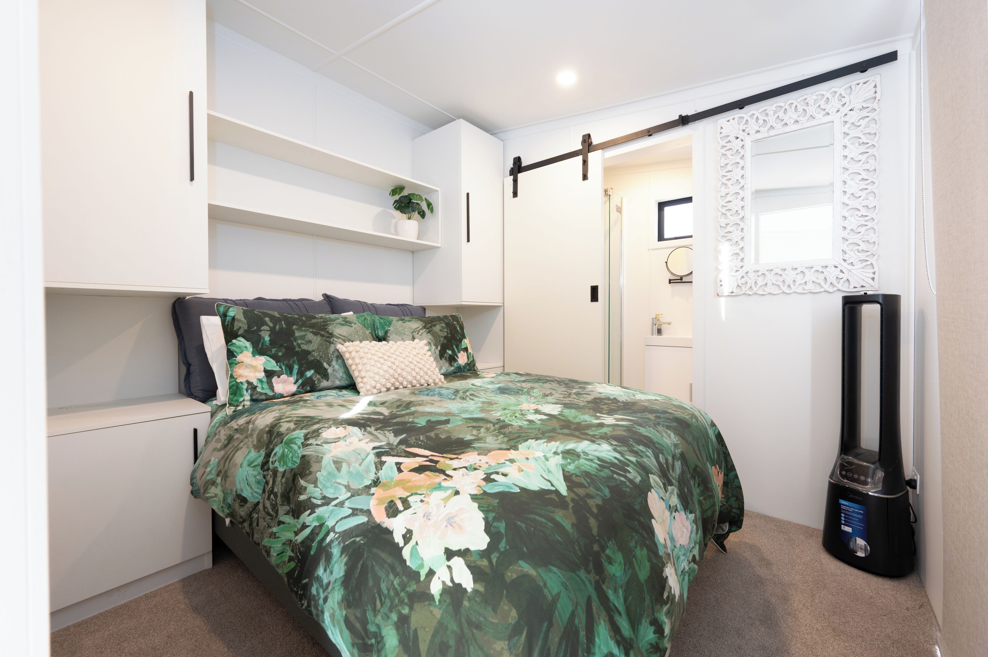 A bedroom with a bed, a shelf with a plant, a wardrobe, and a vacuum cleaner.