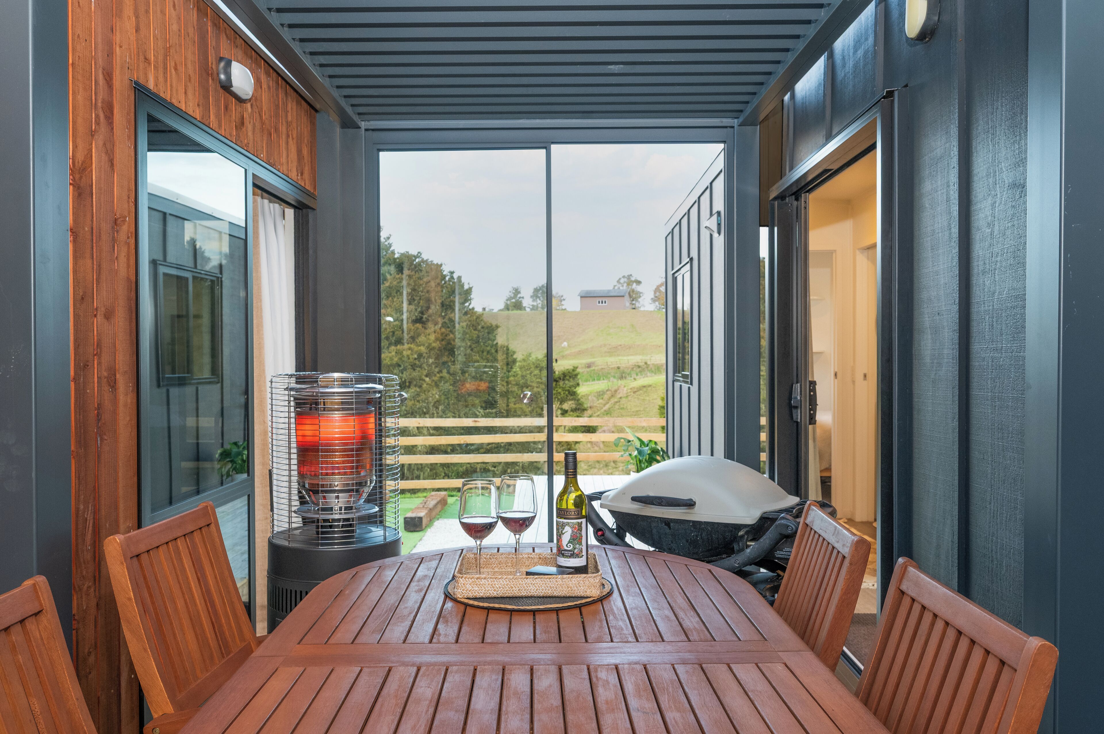 A covered patio with a table set for two, a grill, and a bottle of wine.