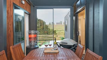 A covered patio with a table set for two, a grill, and a bottle of wine.