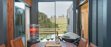 Een overdekt terras met een tafel voor twee, een barbecue en een fles wijn.