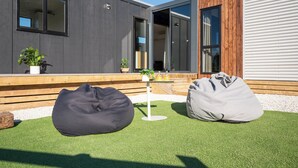 A modern outdoor seating area with two bean bags and a small table with drinks, set against a backdrop of a contemporary building with large windows and a wooden deck.