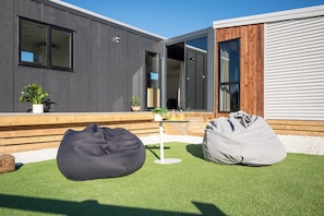 A modern outdoor seating area with two bean bags and a small table with drinks, set against a backdrop of a contemporary building with large windows and a wooden deck.