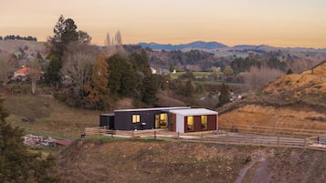 A modern house with a large deck, surrounded by a hilly landscape.