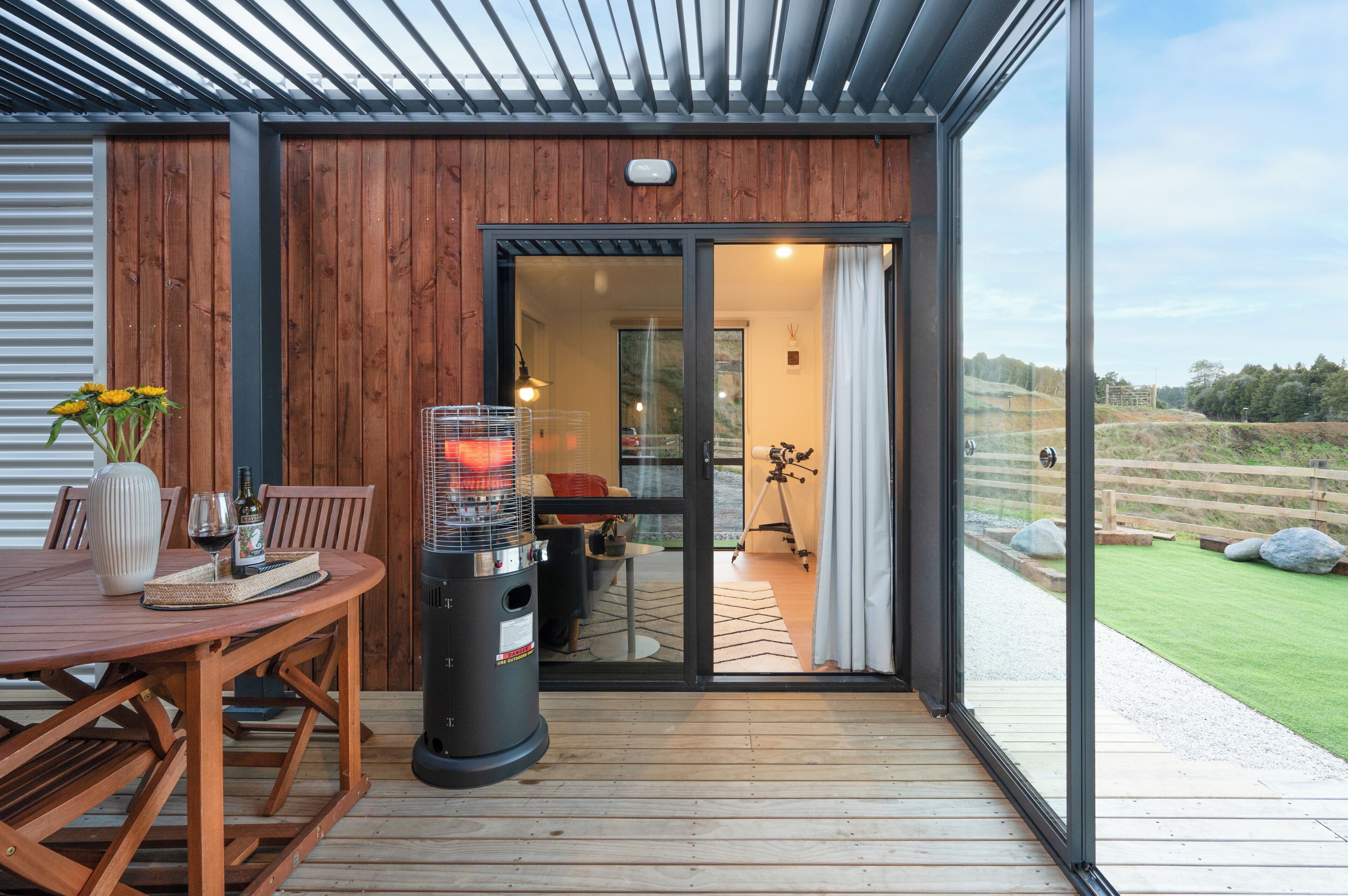 A wooden deck with a table and chairs, a grill, and a view of the outdoors.