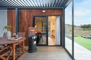 Una terraza de madera con mesa y sillas, una parrilla y vistas al exterior.