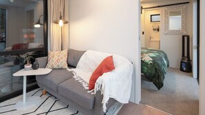 A modern bedroom with a grey sofa, a small white table, and a green bedspread.
