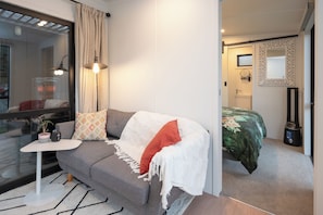 A modern bedroom with a grey sofa, a small white table, and a green bedspread.