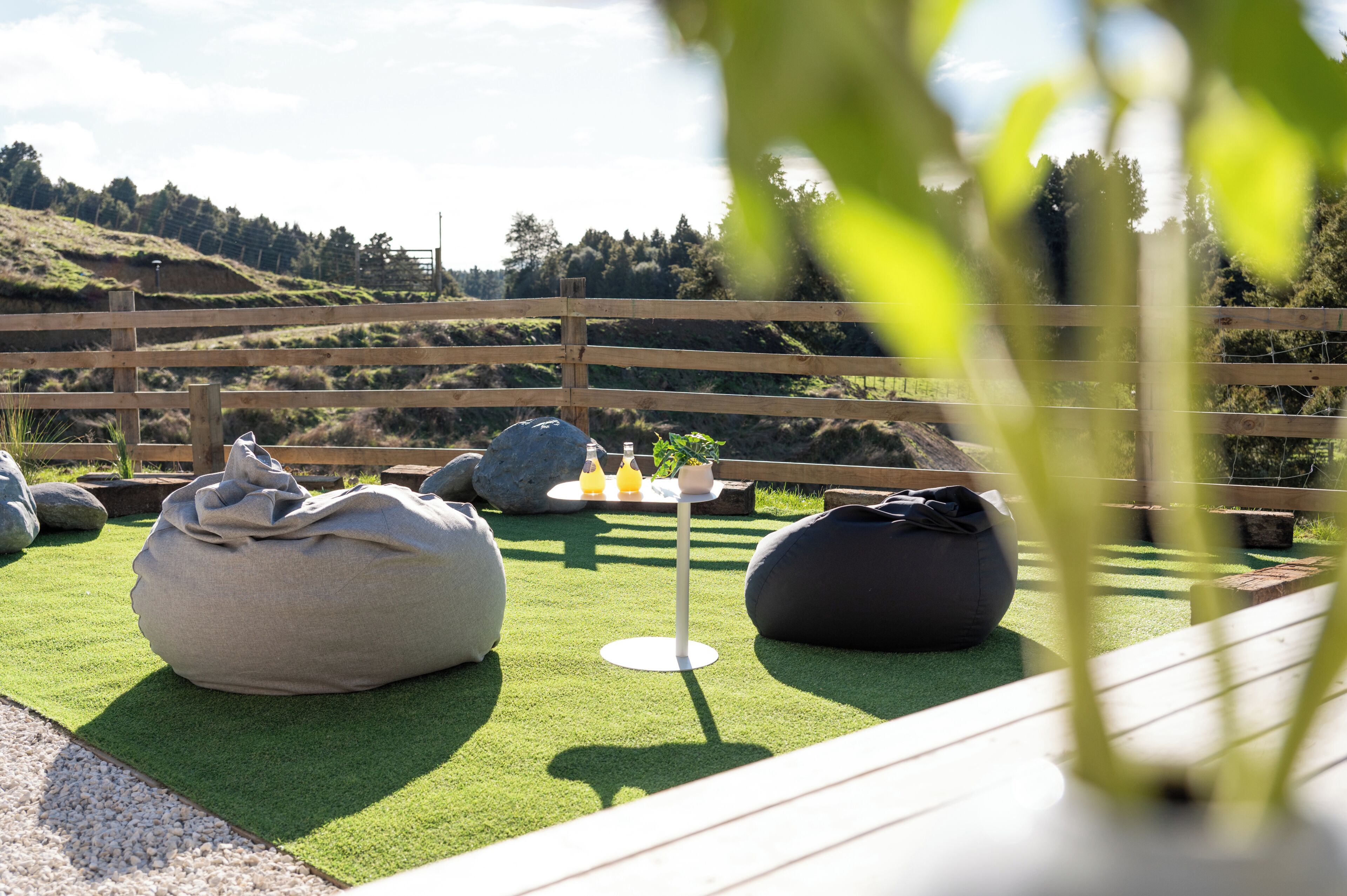 Un área de estar al aire libre con sillones tipo bean bag y una pequeña mesa, rodeada por una cerca de madera y vistas a un paisaje montañoso.