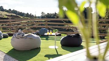 Un área de estar al aire libre con sillones tipo bean bag y una pequeña mesa, rodeada por una cerca de madera y vistas a un paisaje montañoso.