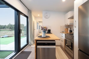 A modern kitchen with a dishwasher, stove, and a clock on the wall. - Haven Hills Retreat - Romantic, luxury off grid tiny house with stunning views. (Taumarunui)