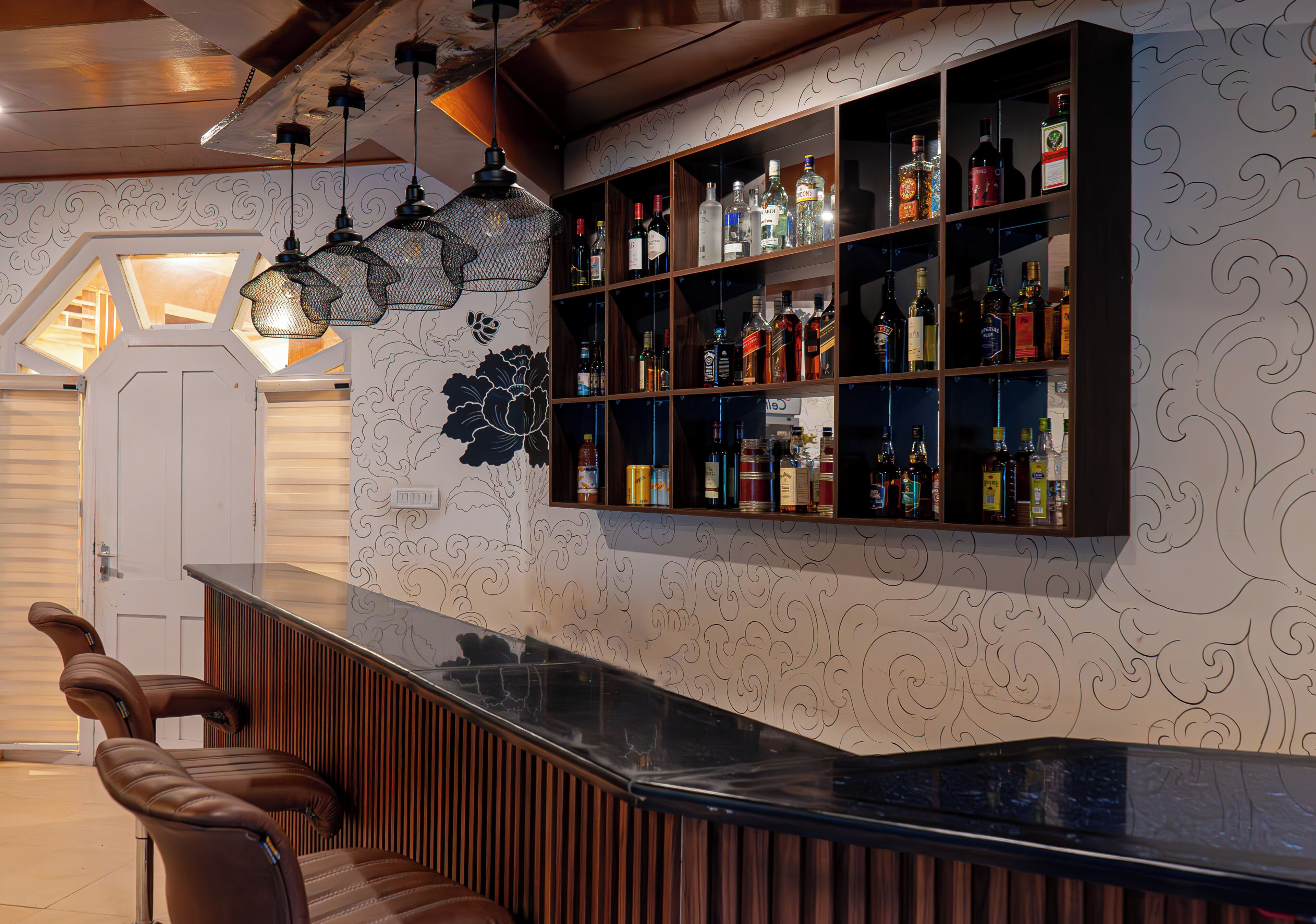 A bar area with a curved counter, multiple shelves of liquor bottles, and a decorative wall with a floral pattern.