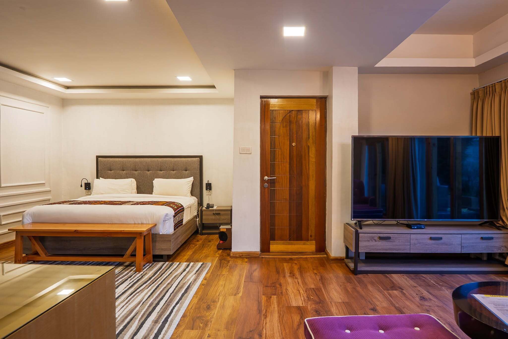A hotel room with a bed, bedside table, TV, and a wooden door.