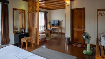 Una habitación de hotel con cama, escritorio con televisor, silla, ventilador y un separador de madera.