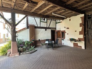 A covered outdoor seating area with brick flooring, wooden beams, and potted plants.