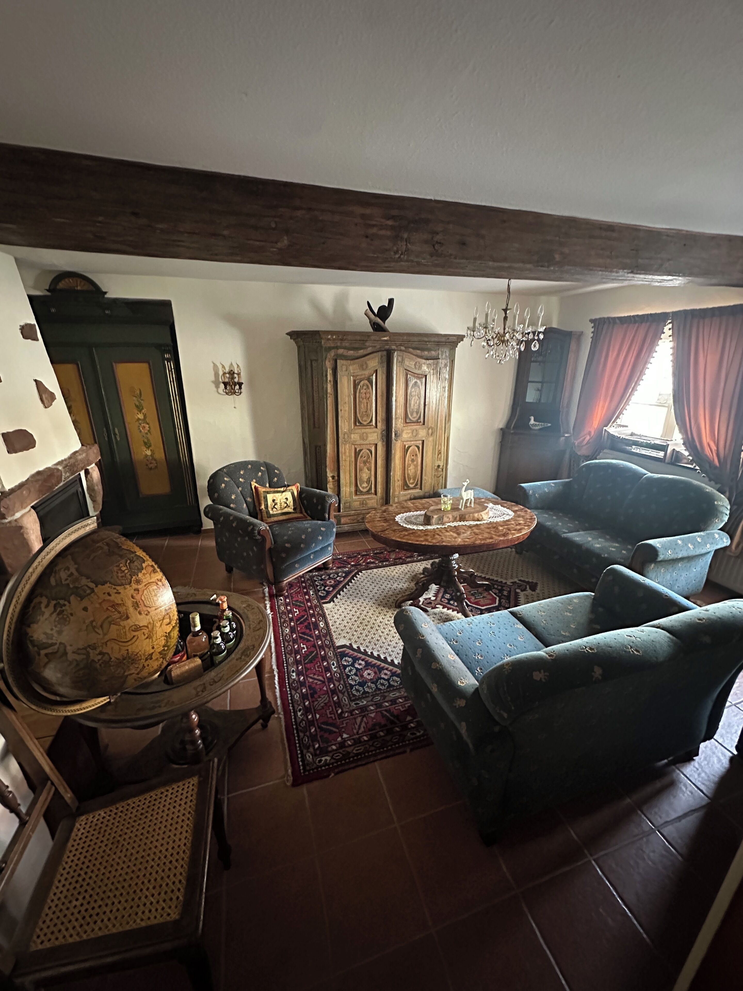 Een klassieke woonkamer met een wereldbol, fauteuils, een houten kast en een getextureerd vloerkleed.