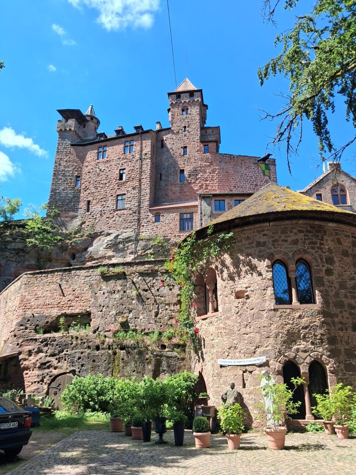 Un château historique en pierre, doté de nombreuses tours et d’une cour intérieure agrémentée de plantes en pot.