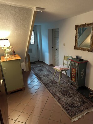 A room with a tiled floor, a chair, a small table with a lamp, a cabinet, and a mirror on the wall.
