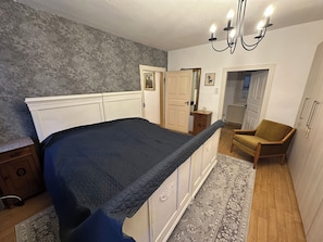 A bedroom with a bed, a nightstand, a chair, a dresser, a mirror, and a chandelier.