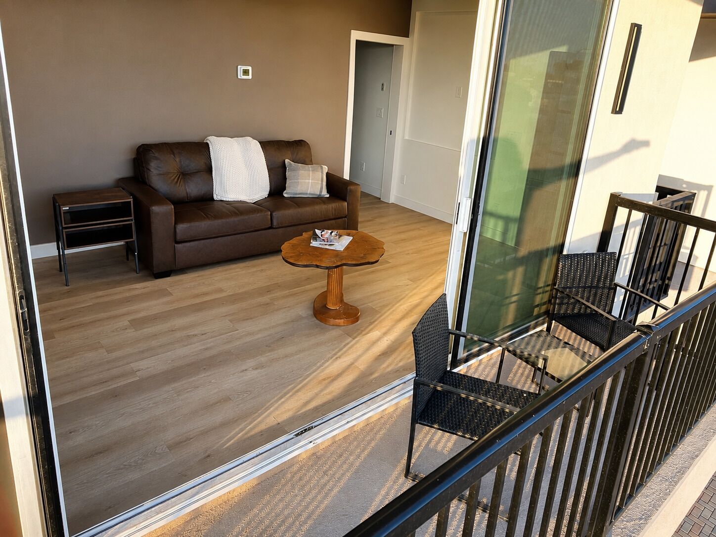 Ein modernes Wohnzimmer mit einem braunen Ledersofa, einem Holztisch und einem Glasgeländer mit Blick auf einen Balkon.