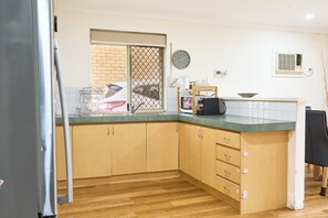 A kitchen with wooden cabinets, a sink, a clock, and a window with a view of a brick wall. - Villa Woody - Your Home Away from Home (Woodbridge)