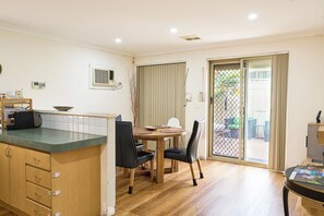 A compact kitchen with a dining area, wooden cabinets, and a sliding glass door leading to an outdoor patio. - Villa Woody - Your Home Away from Home (Woodbridge)