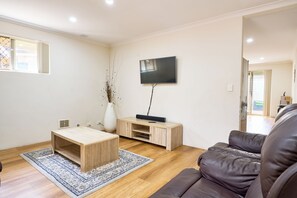 A modern living room with a flat-screen TV, a wooden coffee table, a sofa, and a patterned rug. - Villa Woody - Your Home Away from Home (Woodbridge)