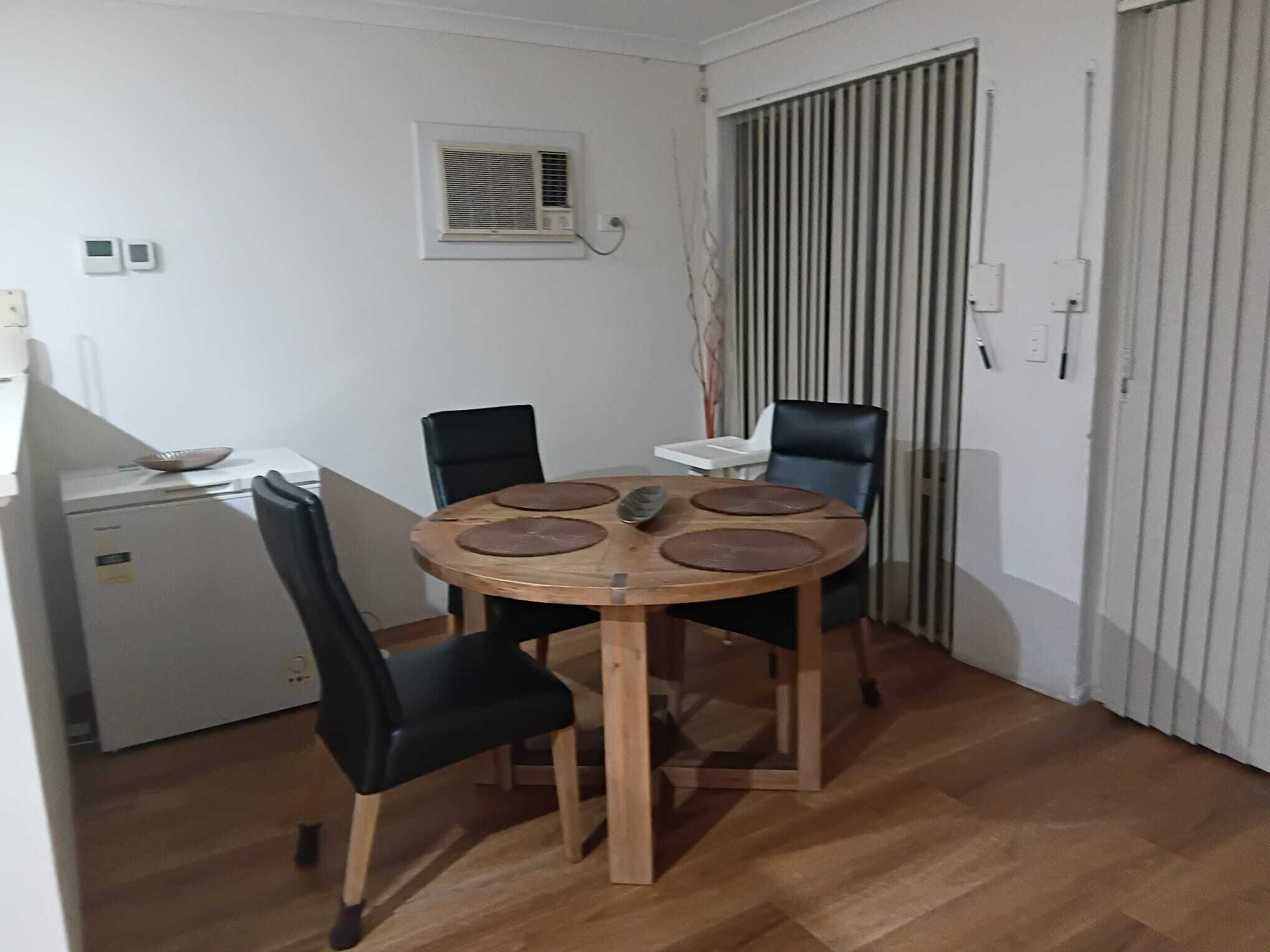 A small dining area with a round wooden table, four chairs, and a refrigerator.