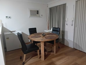 A small dining area with a round wooden table, four chairs, and a refrigerator.