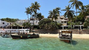 A beachfront with two boats docked, palm trees, and buildings in the background.