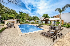 Una piscina con sillas de descanso y un área de patio, rodeada de vegetación y edificios modernos.