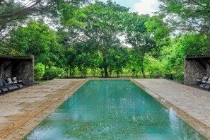 Ein rechteckiger Schwimmteich mit klarem Wasser, umgeben von Steinmauern und üppiger Bepflanzung.