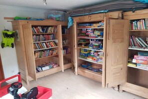 A room with wooden bookshelves filled with books and toys, a red toy car, and a green toy car. - Holiday apartment with 2 bedrooms (Kölpinsee)