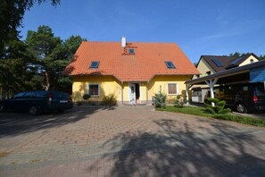 Un edifici de color groc amb teules vermelles, una entrada asfaltada i un porxo cobert.