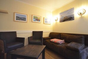 A room with a brown leather sofa, two armchairs, a small wooden table, and three framed pictures on the wall. - Holiday apartment with 2 bedrooms (Kölpinsee)
