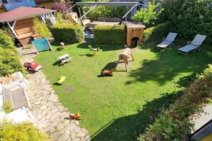 Un pati ben cuidat amb gespa, un espai de joc de fusta, una petita caseta i una zona de seients amb cadires.