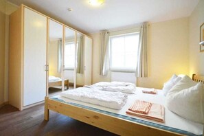 A bedroom with a wooden bed, a large mirror, and a window with curtains. - Holiday apartment with 2 bedrooms (Kölpinsee)