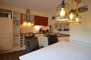 A kitchen with white cabinets, a dining table, and hanging light fixtures. - Holiday apartment with 2 bedrooms (Kölpinsee)