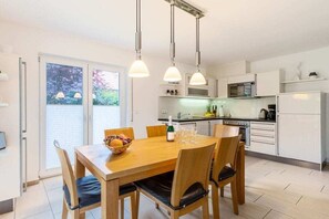 A modern kitchen with white cabinetry, a dining table with chairs, and pendant lighting. - 5-star hotel "Fauna & Flora" (Strasen)
