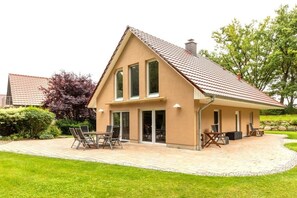 A two-story house with a sloped roof, a patio with outdoor furniture, and a well-maintained lawn. - 5-star hotel "Fauna & Flora" (Strasen)