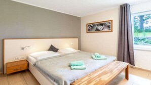 Ein Schlafzimmer mit einem Bett, einem Nachttisch, einer Bank und einem Fenster mit Vorhängen.