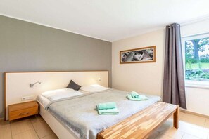 A bedroom with a bed, bedside table, bench, and a window with curtains. - 5-star hotel "Fauna & Flora" (Strasen)