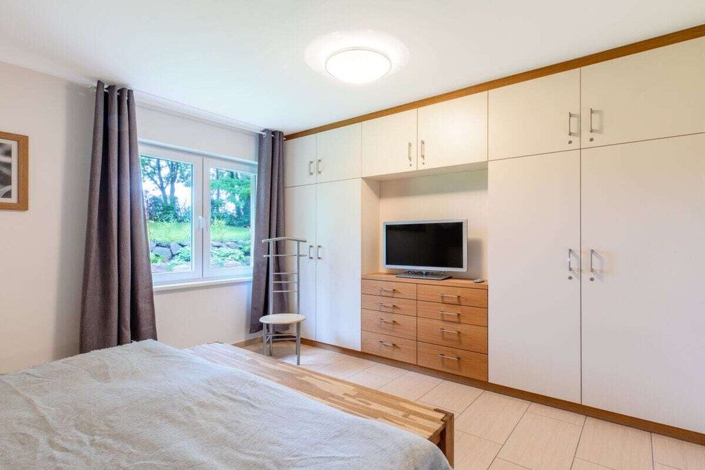 A bedroom with a bed, a TV, a wardrobe, and a window with curtains.