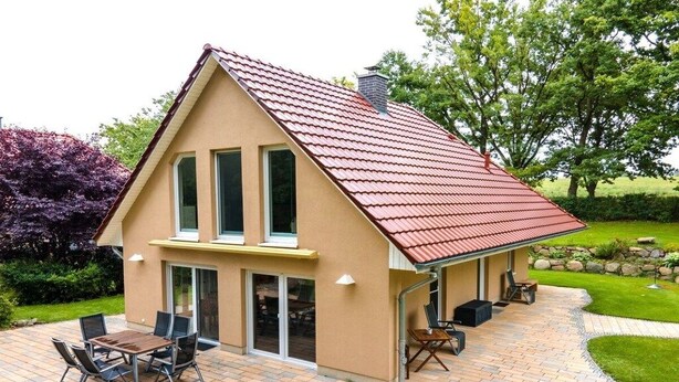 Ein Haus mit rotem Dach, einer Terrasse mit Tisch und Stühlen sowie ein Garten mit Bäumen und Sträuchern.