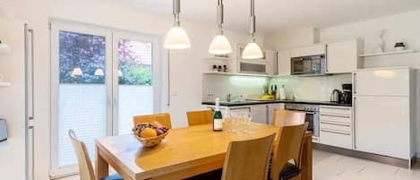 A modern kitchen with white cabinets, a dining table with chairs, and pendant lighting.