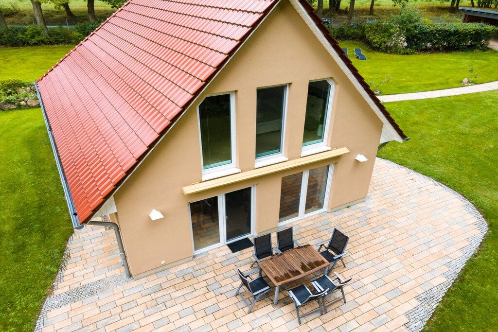A two-story house with a red roof, a patio with a table and chairs, and a lawn.
