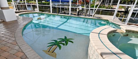 An indoor swimming pool with a tiled edge, a palm tree design, and a view of the surrounding area.