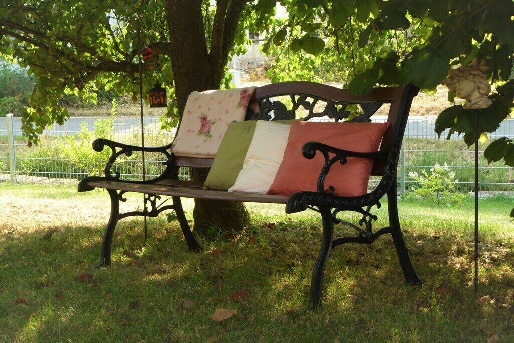 Un banco con un cojín floral y una almohada a rayas verdes y blancas, ubicado bajo un árbol en un parque.